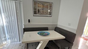 A dining area with a table, bench, ceiling fan, and a framed artwork on the wall. - Penguins on the Beach 2BR Steps to Beach & Downtown, pool,  Unit 7 (Cocoa Beach)