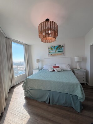A bedroom with a large window, a bed with a green bedspread, two bedside tables with lamps, and a hanging light fixture. - 💎renovated paradise! 10th floorOcean View & lagoon view @ the Palms of Destin🌅🌴 (Destin)