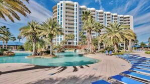 Un resort con una grande piscina, palme e un edificio a più piani con balconi.