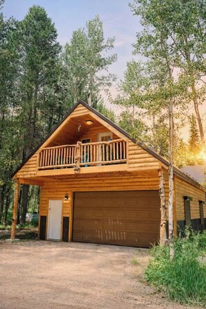 Eine Blockhütte mit Balkon, Garage und einer Auffahrt, umgeben von Bäumen.
