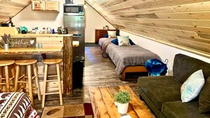 Ein gemütliches Schlafzimmer im Loft-Stil mit einer Küchenzeile, einer Holzbalkendecke und einer kleinen Essecke mit Hocker.