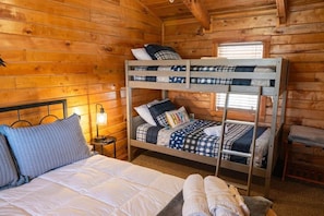 Ein gemütliches Blockhauszimmer mit einem Etagenbett, einem Einzelbett und einem Nachttisch mit Lampe.