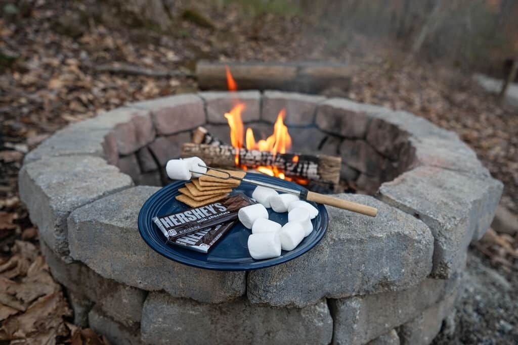 A campfire with marshmallows and chocolate bars on a plate.