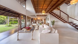 A spacious living area with a wooden staircase, a white sofa, and a coffee table. - Exclusive house in Arraial d'Ajuda: 7 bedrooms, sea view and modern rustic design. (Arraial d'Ajuda)