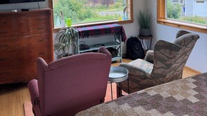 A living room with a large window, wooden furniture, a television, and a view of mountains and trees. - Sleeps 4, close to town. Bayviews! (Homer)