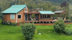A two-story wooden house with a green roof, surrounded by a well-maintained lawn and garden. - Sleeps 4, close to town. Bayviews! (Homer)