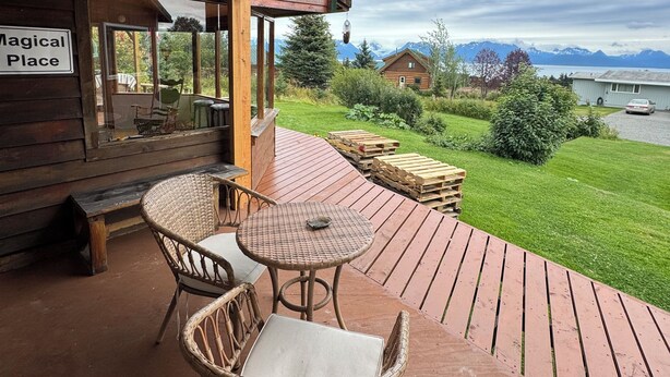 A wooden deck with wicker furniture, a sign reading "Magical Place," and a view of a lake and mountains. - Sleeps 4, close to town. Bayviews! (Homer)