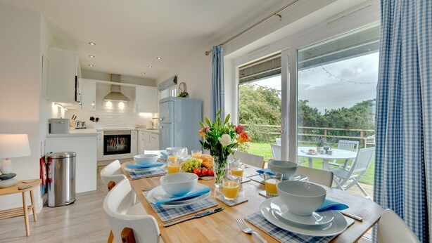 A modern kitchen with white cabinets, a blue refrigerator, and a dining area with a table set for breakfast. - Bumblebee Cottage -  a cottage that sleeps 4 guests  in 2 bedrooms (Filey)