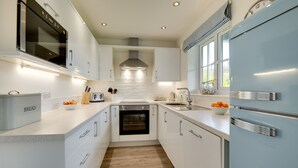 A modern kitchen with white cabinetry, a built-in oven, a refrigerator, and a window with a view. - Bumblebee Cottage -  a cottage that sleeps 4 guests  in 2 bedrooms (Filey)