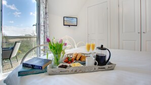 A neatly made bed with breakfast items, a book, and a view of the outdoors. - Bumblebee Cottage -  a cottage that sleeps 4 guests  in 2 bedrooms (Filey)