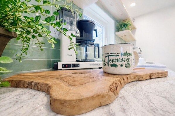 Una encimera de cocina con una cafetera, una taza y una planta.