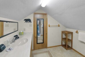 Un baño con lavamanos, espejo, toallero y estante de madera.