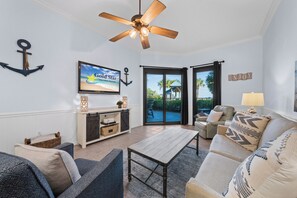 Ein Wohnzimmer mit Deckenventilator, einem Fernseher, der 'Gold Star Vacation Rentals' zeigt, einer Schiebetür, die nach draußen führt, und einem Schild mit der Aufschrift 'ENJOY'.