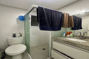 A bathroom with a toilet, sink, and shower. There are towels hanging on a rack, and toiletries on the sink. - Beachfront Apartment in Praia Grande (Praia Grande)