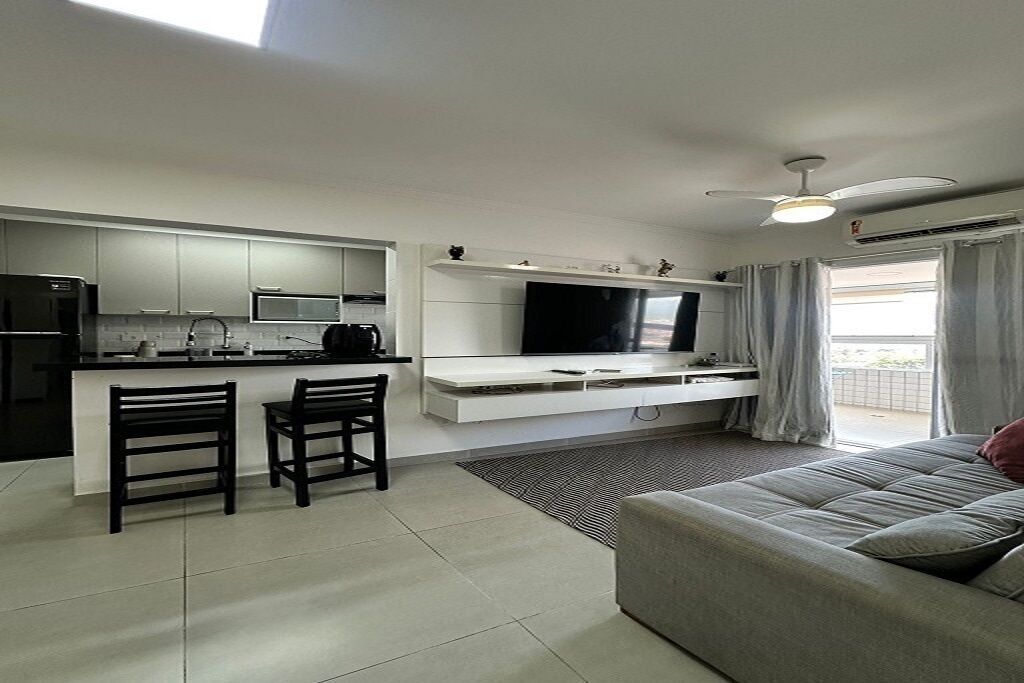 Una cocina moderna con comedor, un televisor de pantalla plana y un balcón con cortinas.