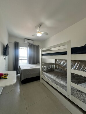 A room with bunk beds, a desk, a television, and an air conditioning unit. - Beachfront Apartment in Praia Grande (Praia Grande)