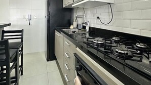Une cuisine moderne avec des murs recouverts de carreaux blancs, un poêle noir et un coin repas comprenant une table et des chaises.
