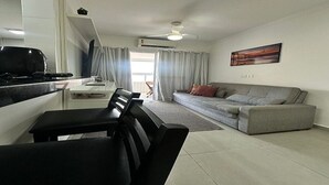 Un salon moderne avec un canapé gris, une table à manger avec des chaises et un coin cuisine équipé d’une cuisinière.