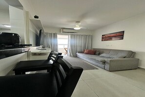 Ein modernes Wohnzimmer mit einem grauen Sofa, einem Esstisch mit Stühlen und einer Küchenzeile mit Herd.