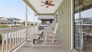Una terraza de madera con sillas mecedoras, bancos, un ventilador de techo y vistas a otros edificios.