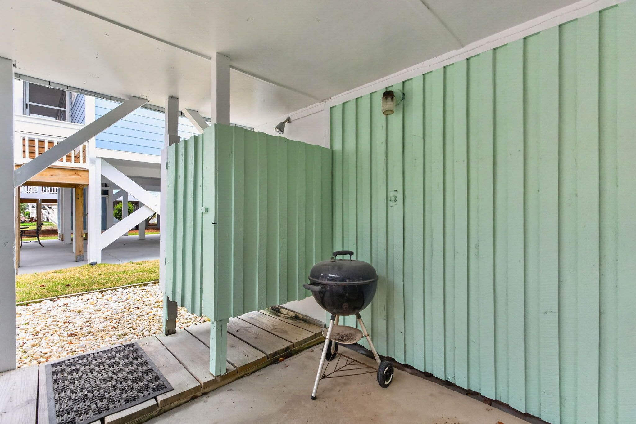 A covered outdoor area with a grill, a metal door, and a staircase leading to an upper level.