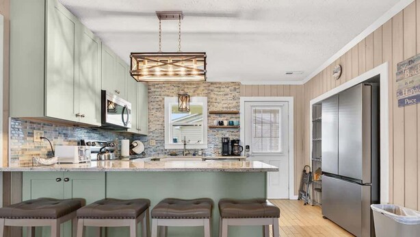 Una cocina con una isla central, taburetes de bar, un refrigerador y una lámpara colgante.