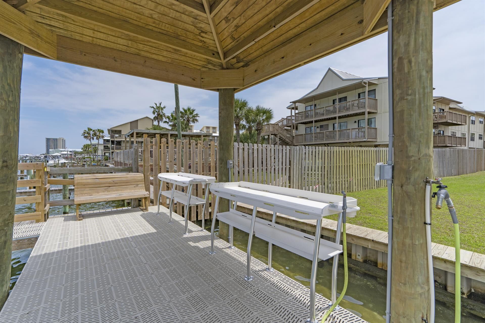 An outdoor seating area with wooden benches and tables, a covered wooden deck, and a view of a residential building with balconies.