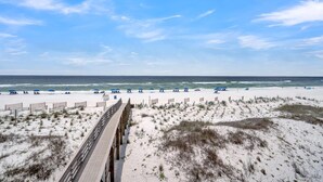 Een strand met een houten promenade die naar de oceaan leidt, zandduinen en strandparasols.