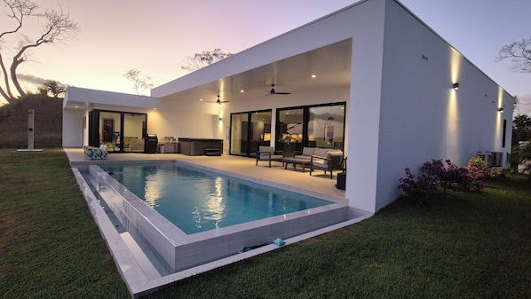 Una casa moderna con piscina, puertas de cristal amplias y mobiliario de exterior.