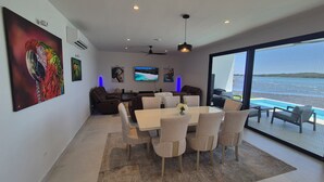 A modern living room with a dining area, large windows, and a view of the sea. - Stunning seaside villa with jacuzzi (Boca Chica)