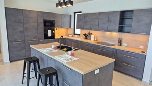 A modern kitchen with dark grey cabinets, a central island with stools, a built-in oven, and a wooden countertop. - Stunning seaside villa with jacuzzi (Boca Chica)