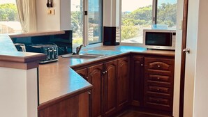 Une cuisine avec des meubles en bois, un four à micro-ondes encastré, un grille-pain et une fenêtre donnant sur un paysage verdoyant.