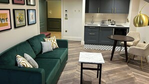 A modern living room with a green sofa, a small table, and a kitchen area with dark cabinets and a round table. - The Hillbrook Sherborne (Sherborne)