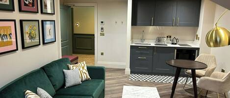 A modern living room with a green sofa, a small table, and a kitchen area with dark cabinets and a round table.