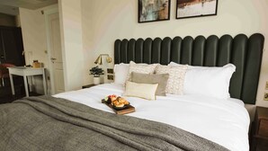 A neatly made bed with a grey blanket, a tray of pastries, and a bedside table with a lamp. - The Hillbrook Sherborne (Sherborne)
