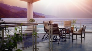 Eine Terrasse mit Tisch und Stühlen, mit Blick auf ein Gewässer und Berge.