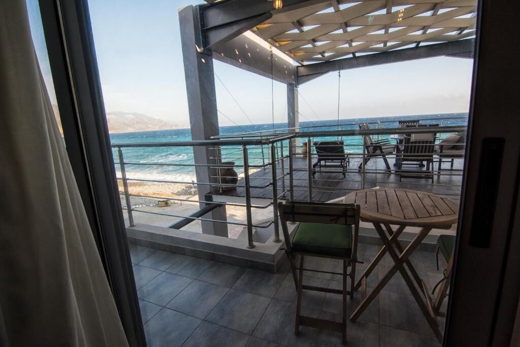 A balcony with a view of the ocean, outdoor seating, and a pergola structure.