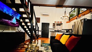 A living room with a black sofa, colorful cushions, a wooden coffee table, and a television. - Lakefront w/ hot tub, firepit, BBQ, smoker, kitchen, patios, king bed, 1.5 bath (Eureka Springs)