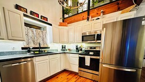 A modern kitchen with stainless steel appliances, white cabinetry, and a wooden floor. - Lakefront w/ hot tub, firepit, BBQ, smoker, kitchen, patios, king bed, 1.5 bath (Eureka Springs)
