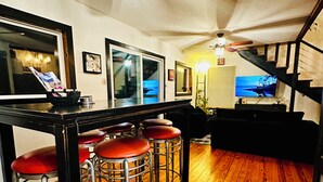 A kitchen with wooden flooring, a bar area with stools, a ceiling fan, and a television. - Lakefront w/ hot tub, firepit, BBQ, smoker, kitchen, patios, king bed, 1.5 bath (Eureka Springs)