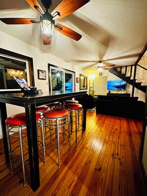 A kitchen with wooden flooring, a bar area with stools, a ceiling fan, and a television. - Lakefront w/ hot tub, firepit, BBQ, smoker, kitchen, patios, king bed, 1.5 bath (Eureka Springs)