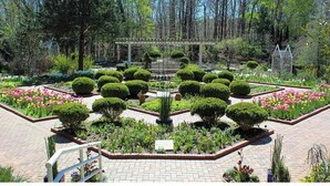 Un jardín formal con arreglos de topiaria simétricos, una pérgola central y una variedad de plantas florecientes.