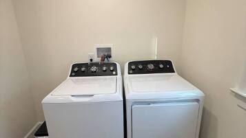 A laundry room with two white front-loading washing machines and a small shelf with a few items.