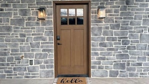 A stone wall with a wooden door, two wall-mounted lanterns, and a doormat with the word "hello". - Golden Glow Getaway (Myerstown)