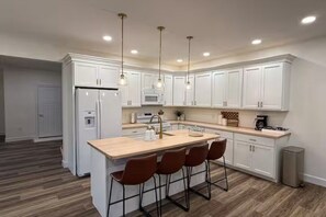 A modern kitchen with white cabinetry, a central island with bar stools, and pendant lighting. - Golden Glow Getaway (Myerstown)