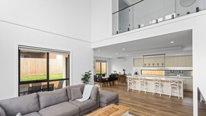 A spacious living area with a grey sofa, a dining table, and a kitchen with white bar stools. - Spacious Central 2 story Luxury with views (San Remo)