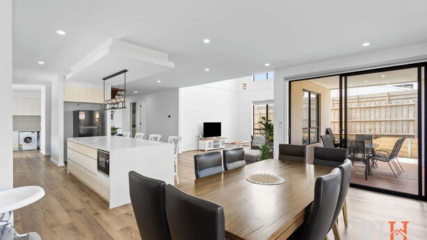 A modern kitchen with a central island, a dining area with a wooden table and chairs, and a sliding glass door leading to a patio. - Spacious Central 2 story Luxury with views (San Remo)