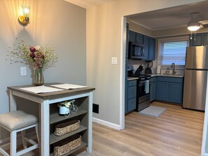 A modern kitchen with blue cabinets, a stainless steel refrigerator, and a dining area with a vase of flowers.