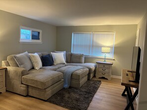 A living room with a sectional sofa, a small side table, a lamp, and a TV stand.