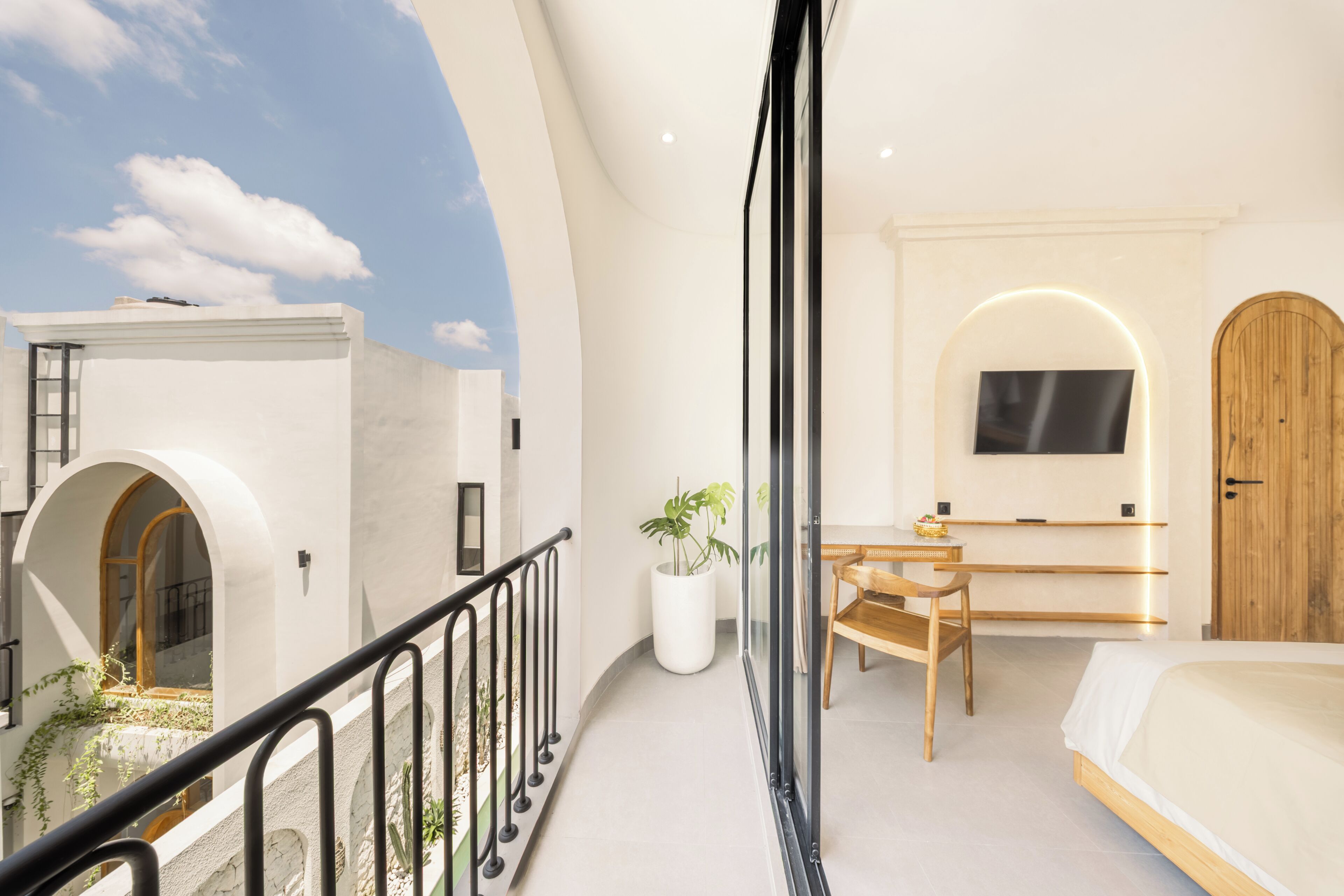 A modern bedroom with a bed, a TV, a wooden door, and a balcony with a railing.
